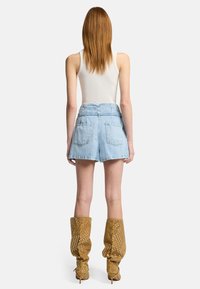 Pantalones cortos de mezclilla azul claro de cintura alta con cintura ceñida, que cuentan con bolsillos traseros. Combinados con botas de mostaza perforadas hasta la rodilla.