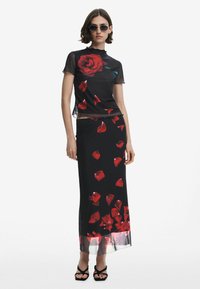 Schwarzes Zweiteiler-Outfit mit einem transparenten Oberteil, das mit einem großen roten Rosenmotiv versehen ist, und einem Rock mit verstreuten roten Blütenblatt-Designs.