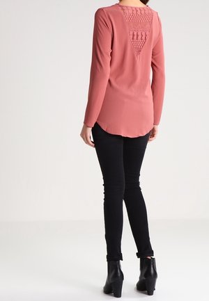 Blusa rosa pallido a maniche lunghe con dettaglio a V testurizzato sulla schiena, abbinata a jeans neri aderenti e stivaletti con tacco.
