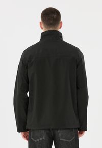 Svart jacka med hög krage, platta sömmar och avslappnad passform. Tillverkad av ett mjukt, vattentåligt material. Har ingen synlig hårdvara.