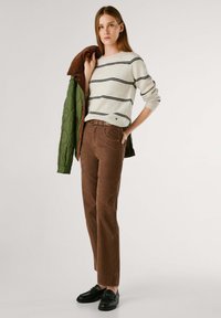 Bruine corduroy broek met een rechte pasvorm, gecombineerd met een crèmekleurige gestreepte trui en een groene gewatteerde jas. Zwarte schoenen maken de outfit compleet.