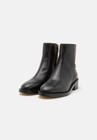Bottes montantes en cuir noir à finition lisse, dotées d'une fermeture éclair dorée et d'un accent marron texturé sur le talon. Design à talon bloc.
