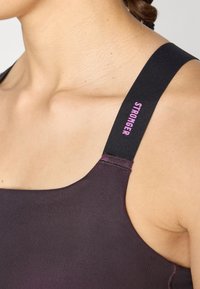 Melnā sporta tops ar regulējamiem siksniņām. Iespējas ar rozā "STRONGER" drukājumu uz siksniņas, gluda auduma un pieguļoša dizaina.