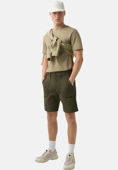 Herren Olivgrüne Shorts mit mehreren Taschen, kombiniert mit einem beigen T-Shirt und einer hellen Mütze. Hat ein lässiges Design und eine bequeme Passform.