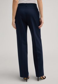 Marineblaue gerade geschnittene Hosen mit einem strukturierten Bund, Gesäßtaschen und einer glatten Oberfläche, kombiniert mit schwarzen High Heels.