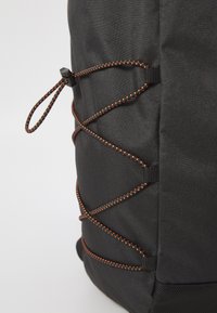 Black fabric backpack featuring an elastic bungee cord design with orange accents, reinforced seams, and a textured finish.