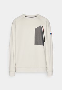 Light beige sweatshirt with a textured black pocket. Features raglan sleeves, a rounded neckline, and a small logo on the sleeve.