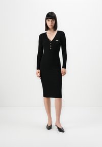 Black ribbed knit dress with long sleeves, V-neck, gold button details, and a small accent pin. Knee-length with a fitted silhouette.