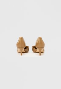 Lysebrune højhælede sko med glat læderfinish, spids tå og slanke hæle. Har en cirkulær detalje bagpå.