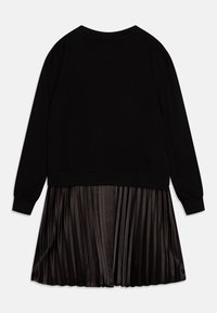 Schwarzes Sweatshirt mit langen Ärmeln, kombiniert mit einem gefalteten schwarzen Rock. Glatte Stoffoberfläche mit einem gerippten Ausschnitt und Bündchen.