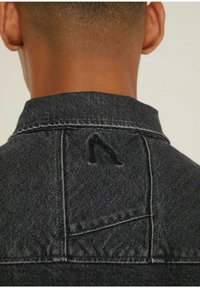 Giubbotto in denim nero con colletto strutturato, cuciture visibili e logo ricamato sul girocollo. Texture liscia e vestibilità sartoriale.