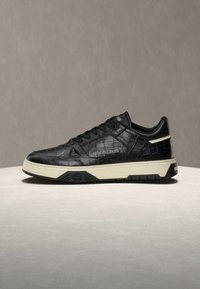 Baskets noires en cuir synthétique façon crocodile avec semelle blanche, logo latéral "roberto cavalli," et lacets noirs sur une surface claire unie.