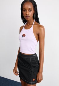 Top corto halter viola chiaro con ricami di rose, abbinato a una mini gonna nera aderente con cuciture bianche e un'etichetta con logo.
