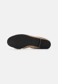 Beige suede såle med en teksturert svart gummiyttersåle, som har spor for grep og et avrundet tådesign.