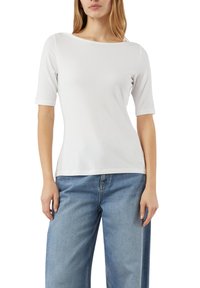 Biały top z krótkim rękawem wykonany z miękkiego materiału, z dekoltem w łódkę i dopasowanym krojem, zestawiony z jasnoniebieskimi, szerokimi dżinsami.