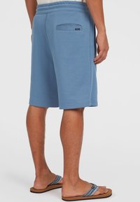 Shorts bleu clair en tissu doux avec une taille élastique, dotés d'une poche arrière et d'une coupe droite, associés à des tongs marron.