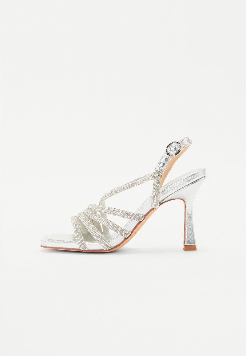 Silberne High Heels Sandalen mit mehreren glitzernden Riemen, offener Zehenpartie und Slingback-Stil. Glatte Textur mit metallic-finish.