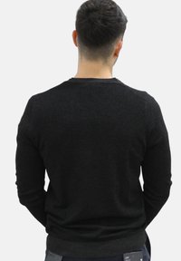Zwarte gebreide trui met een ronde hals en lange mouwen, met een gladde textuur en geribbelde manchetten, gezien van de achterkant.