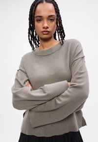 Szary sweter robiony na drutach z okrągłym dekoltem, z długimi, opadłymi rękawami i luźnym krojem. Materiał jest miękki o gładkiej fakturze.