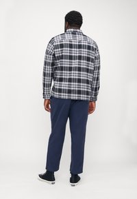 Plaid shirt in black and white with a button collar, paired with navy pants and black sneakers. View from the back, highlighting the shirt's pattern.