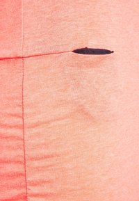 Koralowo-różowa tkanina o miękkiej fakturze z małym czarnym przeszyciem po bokach. Widoczne są detale szwów, które podkreślają design.