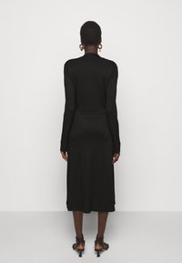 Černé žebrované úpletové šaty s dlouhým rukávem, těsně přiléhající v pase a midi délky, s kulatým výstřihem a bočním rozparkem na spodním lemu.