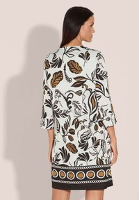 Blumenkleid mit weißem Hintergrund und schwarzen sowie braunen Blattmustern, mit Dreiviertelärmeln und einer dekorativen Bordüre am Saum.