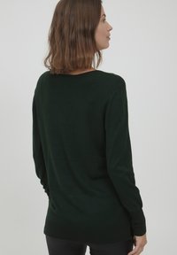 Mørkegrøn sweater med lange ærmer, afslappet pasform og ribbet kant ved hæm og manchetter. Blødt stof med en glat tekstur og minimale sømme.