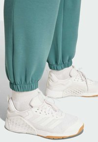 Türkise Jogginghosen mit elastischen Bündchen, kombiniert mit weißen Sportschuhen mit Mesh- und Gummidetails. Texturiertes Socken über den Schuhen sichtbar.