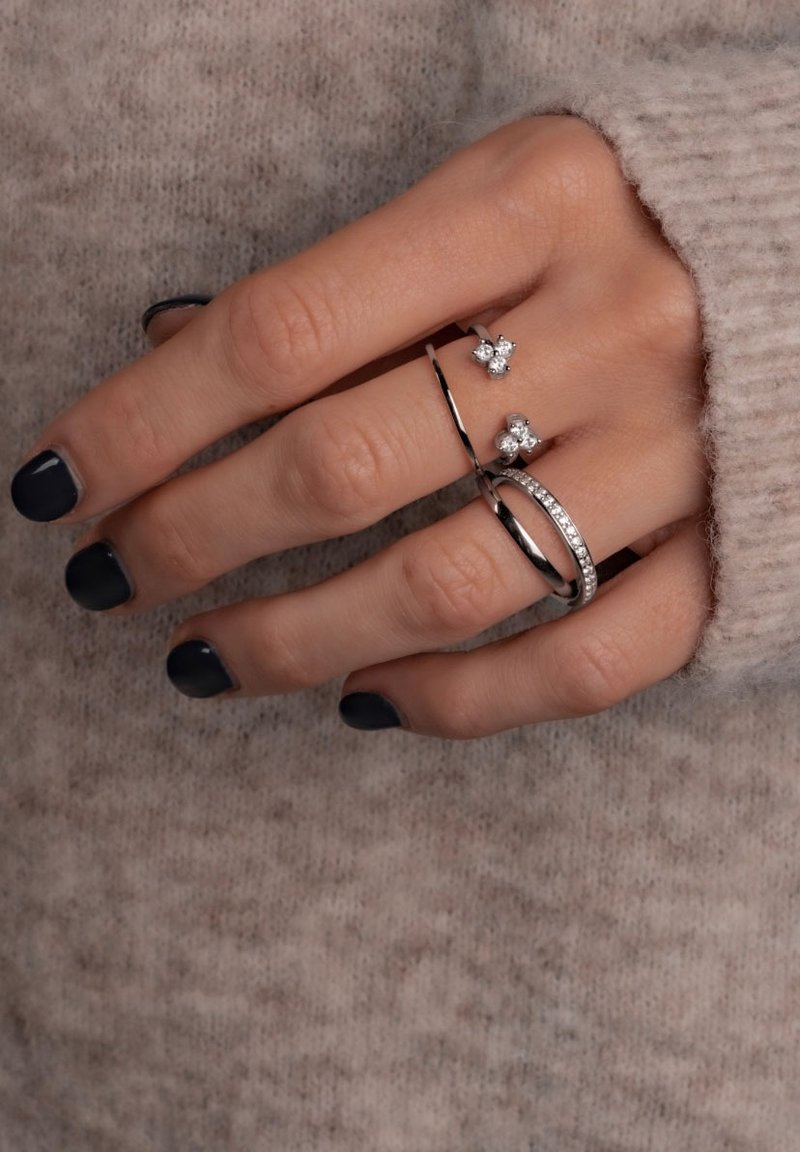 Három ezüstgyűrű egy kézen bemutatva. Az egyik kis gyémánt díszítésekkel rendelkezik, a másik sima sávval bír, a harmadikat pedig egy sor kő díszíti.