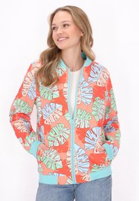 Giubbotto bomber colorato con uno sfondo corallo che presenta ampi motivi di foglie verdi e blu. Chiusura con zip, tasche interne e polsini a coste.
