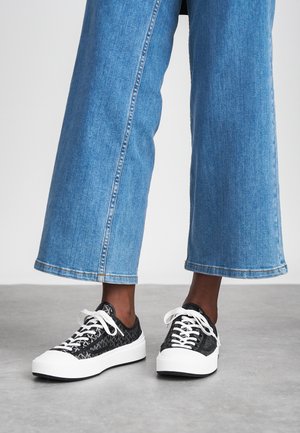Svarte mønstrede sneakers med hvite snørebånd, med en tykk hvit såle. Brukt med vide blå denimbukser.