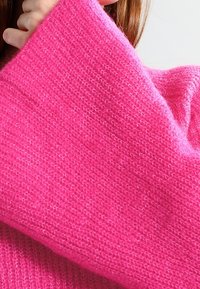 Pull en maille fuchsia à manches larges, avec un tissu doux et texturé et une coupe ample et décontractée.