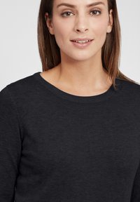 Maglione nero a maglia con scollo rotondo, texture liscia e una leggera brillantezza. Presenta un design aderente e dettagli minimal.