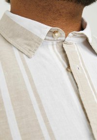 Beżowo-biała koszula w paski z wyrazistym kołnierzykiem, pojedynczym zapięciem na guzik oraz miękkim, teksturowanym materiałem.