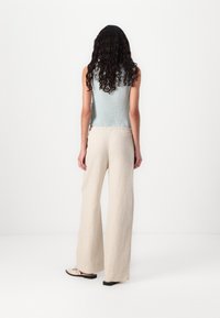 Top senza maniche di un blu chiaro, abbinato a pantaloni larghi in lino color crema. L'outfit presenta una vestibilità comoda e un tessuto testurizzato. Scarpe nere e beige.