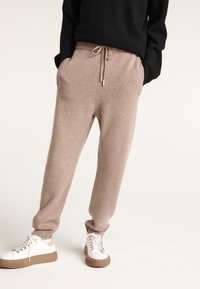 Helle beige Strick-Jogginghosen mit Seitentaschen, elastischem Taillenbund und verstellbarem Kordelzug, kombiniert mit weißen Turnschuhen und neutralen Sohlen.