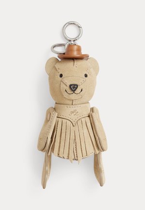 Porte-clés ours en daim beige portant une robe à franges et un petit chapeau en cuir marron attaché à un anneau en argent.