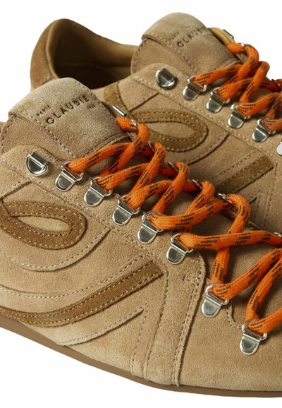 Baskets en daim beige avec des lacets orange à motifs, des œillets métalliques et des coutures détaillées sur les côtés et la languette.
