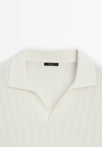 Pull en maille côtelée blanche avec un large col et une ouverture en V, doté d'une étiquette noire cousue à l'intérieur de l'encolure.