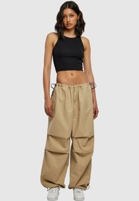 Top court noir associé à un pantalon cargo beige ample avec une taille élastique et des cordons de serrage, porté avec des baskets blanches.