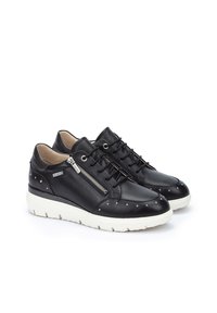 Zapatillas de cuero negro con tachuelas plateadas, cremallera lateral y suela de goma blanca. Presentan un diseño de cordones y una textura suave.