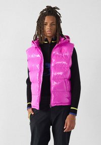 Gilet imbottito lucido di colore rosa acceso con cappuccio, caratterizzato da sezioni trapuntate e cerniera frontale. Indossato sopra una maglia nera a maniche lunghe.