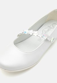 Weißes Ballettschuh mit einer runden Zehe, ausgestattet mit einem silbernen Riemen, der mit kleinen, bunten Blumenakzenten verziert ist. Glatte Ledertextur.