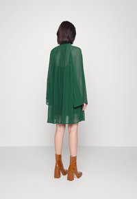 Zielona, plisowana sukienka z długimi rękawami, zwiewny materiał i dół sięgający powyżej kolan. Połączona z błyszczącymi, brązowymi botkami za kostkę.