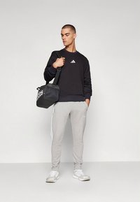 Svart sweatshirt med vitt Adidas-logotyp, grå joggingbyxor med vita ränder och en svart gymväska, bärs med vita träningsskor.