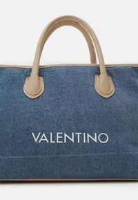 Džínová taška přes rameno s béžovými koženými držadly, s stříbrným logem "VALENTINO" na přední straně. Strukturovaný tvar se šitými detaily.