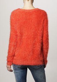 Fuzzy, vibrande orange tröja med lös passform, rund halsringning och långa ärmar, tillverkad av mjukt, texturerat tyg, synlig bakifrån.