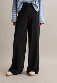 Pantalons larges noirs en tissu doux, avec une taille élastique. Associés à un haut bleu à rayures à manches longues et à des baskets claires.