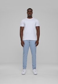 T-shirt bianca a maniche corte abbinata a jeans aderenti azzurri e sneakers bianche. Design semplice con scollo rotondo e texture liscia.